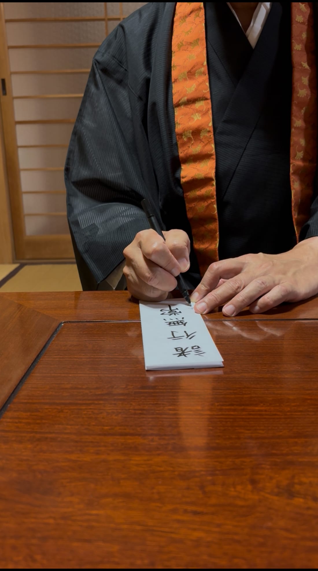 短冊に筆で言葉を記す住職